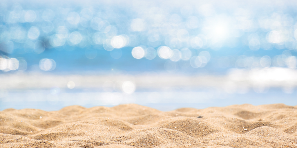 Sunlit beach sand with a shimmering ocean bokeh background, perfect for summer activities.