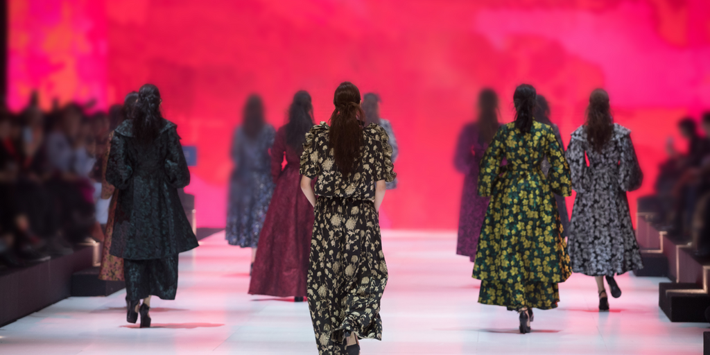 Models in floral dresses walk the runway at New York Fashion Week, showcasing bold prints in sustainable materials.