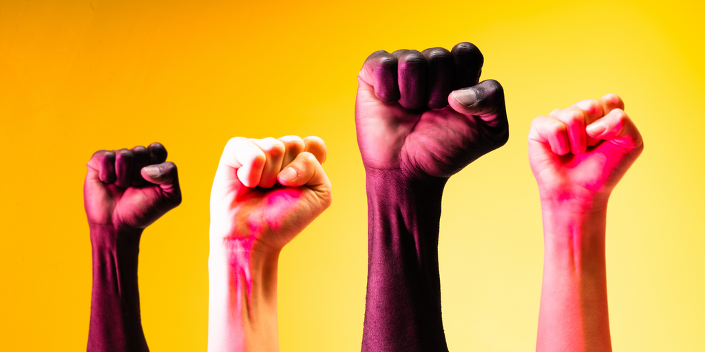 Four raised fists in the air against a yellow background, symbolizing solidarity and activism.